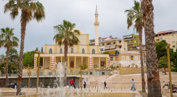 Fontanna i palmy przed meczetem w Durrës, Albania. Ludzie spacerują po placu.
