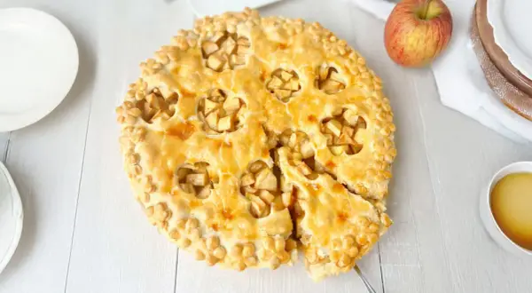 Goldbrauner Apfelkuchen mit Blätterteig-Dekor, ein Stück herausgeschnitten.