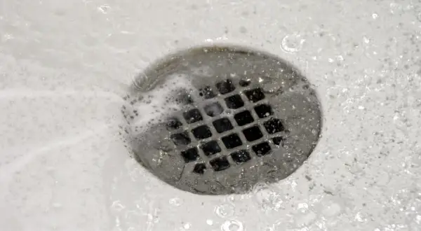 Acqua e schiuma scorrono nello scarico della doccia, un segno che il lavoro di pulire scarico doccia è stato fatto.