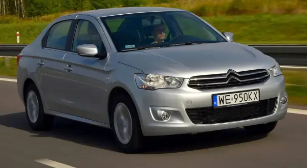 Srebrny Citroen C Elysee jedzie po drodze, za kierownicą siedzi mężczyzna.