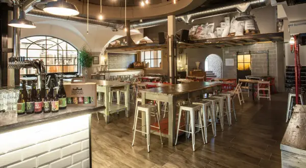 Interno del birrificio Legnano con tavoli, sgabelli e birre in bottiglia sul bancone.