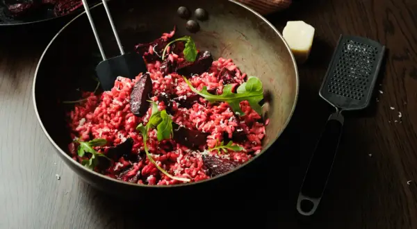 Un délicieux risotto betterave, garni de roquette fraîche et de copeaux de parmesan, prêt à être dégusté.