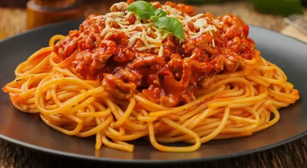 Pyszne spaghetti z mięsem mielonym w sosie pomidorowym, posypane serem i udekorowane bazylią. Idealny prosty przepis na obiad.