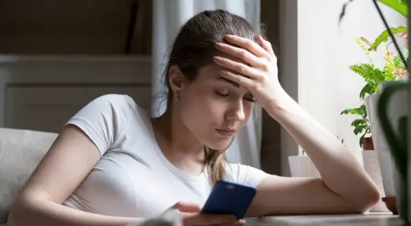 Zamyślona kobieta z ręką na czole, patrząca na telefon. Może to znak, po czym poznać, że ona chce odejść.