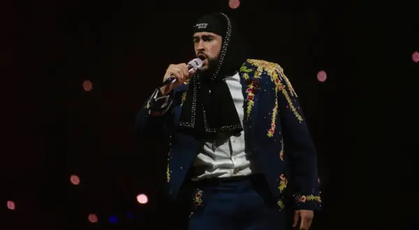 Bad Bunny koncert: artysta w ozdobnej marynarce i czapce z napisem "Puerto Rico" śpiewa do mikrofonu na tle rozmytych świateł.