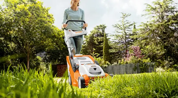 Mujer cortando césped con cortacésped eléctrico. Consejos para cortar el césped: mantén la cuchilla afilada y la altura adecuada.