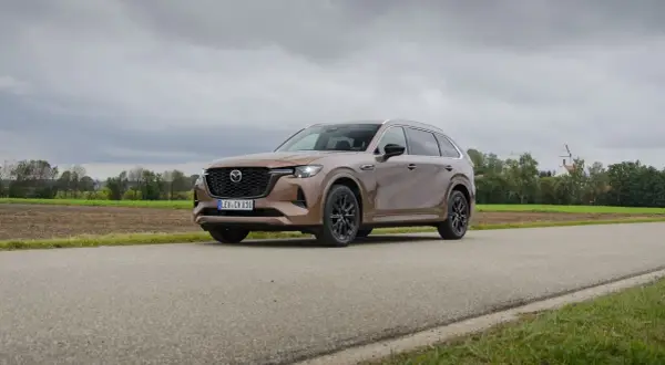 Brązowa Mazda CX80 na tle wiejskiego krajobrazu z kościołem w oddali.