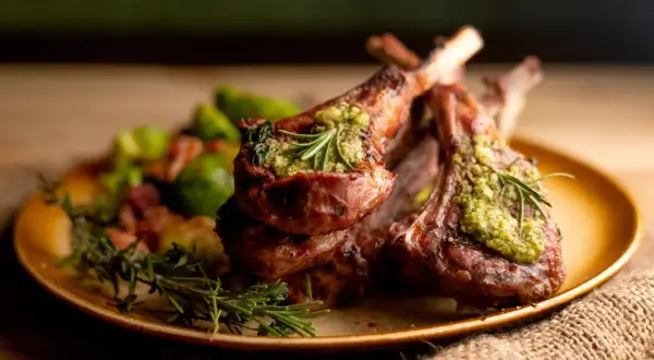 Costillas de cordero asadas con pesto y romero, acompañadas de verduras. Un plato de cordero para recetas gourmet.
