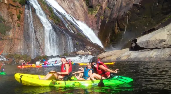 Familia disfrutando en kayak frente a la impresionante fervenza de Ézaro, con cascadas cayendo sobre rocas.