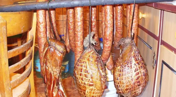 Wędzone mięsa wiszą na drążku. Widać kiełbasy i wędzonki, w tym boczek, który wygląda jakby był przygotowany z użyciem marynaty do boczku.