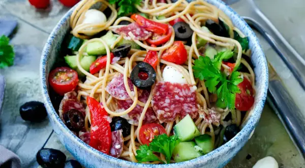 Spaghetti-Salat mit Salami, Tomaten, Oliven und Mozzarella. Ein einfach und schnell zubereitetes Gericht, perfekt für heiße Tage.
