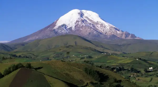 Ośnieżony wulkan Chimborazo, który jest najwyższą górą na świecie od środka Ziemi. W dole zielone wzgórza i pola.