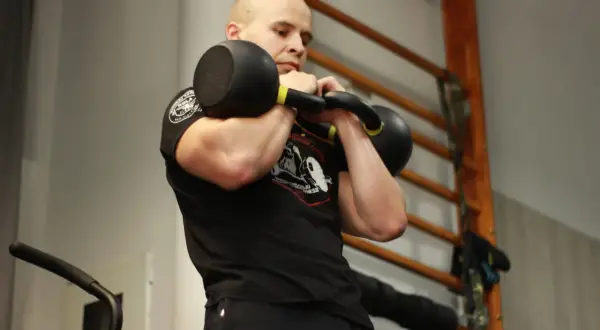 Mężczyzna ćwiczy z kettlebell, pokazując, jakie partie mięśni ćwiczyć razem dla efektywnego treningu.