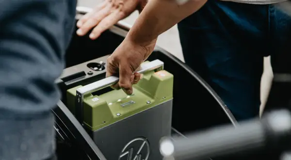 Ręce wyjmują zieloną baterię z pojazdu elektrycznego. Czy świadectwo sprawności baterii w autach EV stanie się obowiązkowe przy przeglądzie?