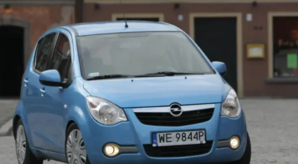 Niebieski Opel Agila 1.2 na brukowanej ulicy przed budynkiem.