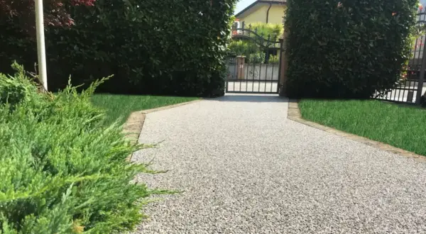 Vialetto carrabile in pietra, con ghiaia chiara e bordi in cotto, conduce a un cancello in ferro battuto.