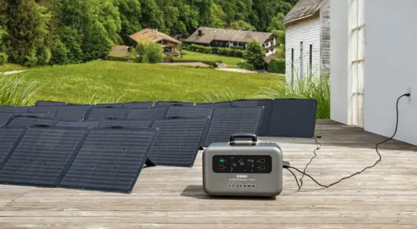 Instalación de baterías solares en un porche de madera, con paneles solares desplegados y una unidad de energía portátil conectada a una casa.