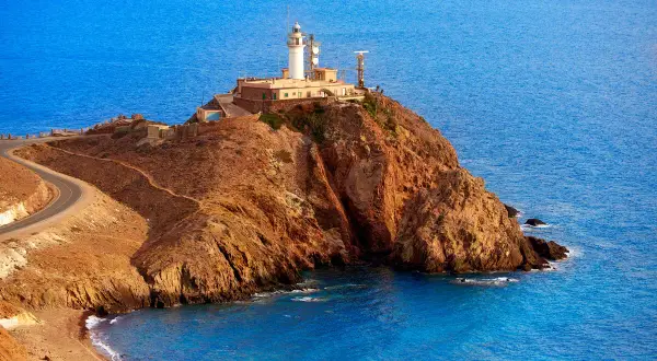 Faro en un acantilado rocoso con el mar azul de fondo. Un camino serpentea hacia la cima. ¡Un lugar perfecto para ver Cabo de Gata!