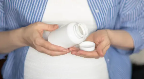 Kobieta w ciąży trzyma białą buteleczkę i jej nakrętkę. Rozważa, czy wziąć paracetamol w ciąży.