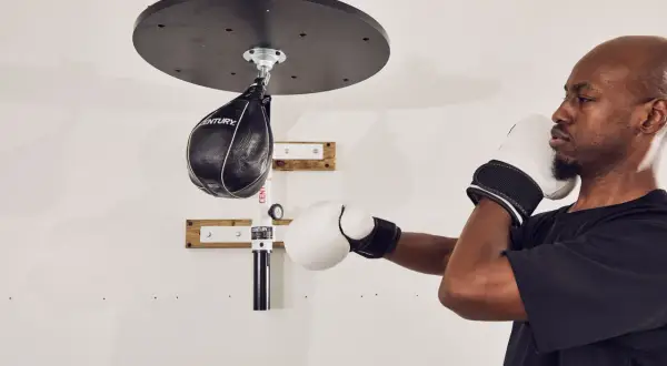 A man in boxing gloves trains with a speed bag, proving a speed bag is a good workout for reflexes and endurance.