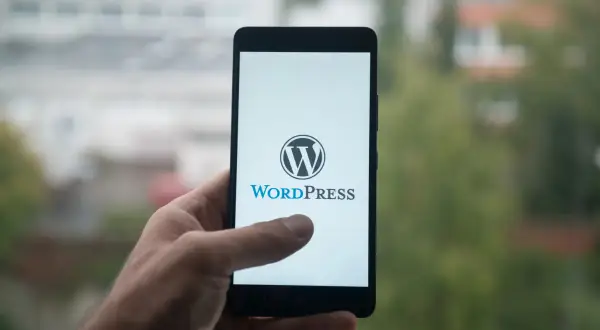 Dłoń trzyma smartfon z logo WordPress. Idealne narzędzie dla webmasterów do zarządzania stronami.