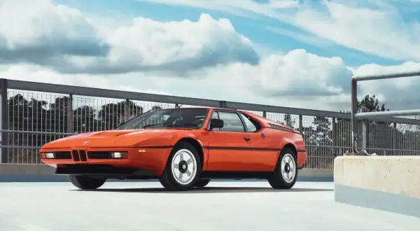 Pomarańczowy klasyk BMW E26 na tle nieba z chmurami.