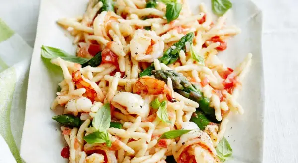 Trofie-Pasta mit Garnelen, Spargel und Tomaten, garniert mit Basilikum.