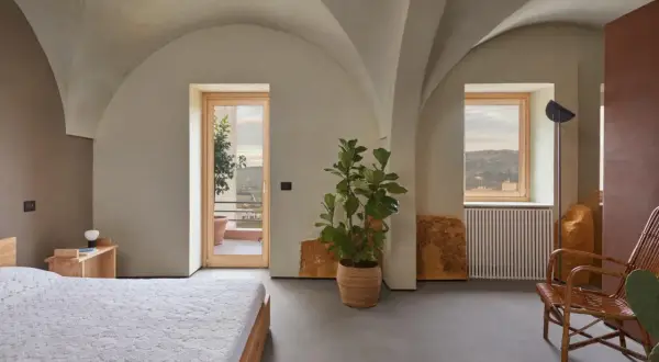 Interno moderno con soffitti a volta, letto, pianta e vista panoramica. Sembra una di quelle case a un euro che diventano gioielli.