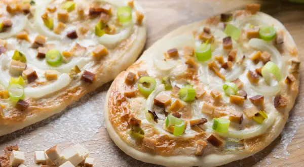 Zwei knusprige, vegetarische Flammkuchen mit Zwiebeln, Frühlingszwiebeln und würzigen Tofuwürfeln, bestreut mit etwas Mehl.