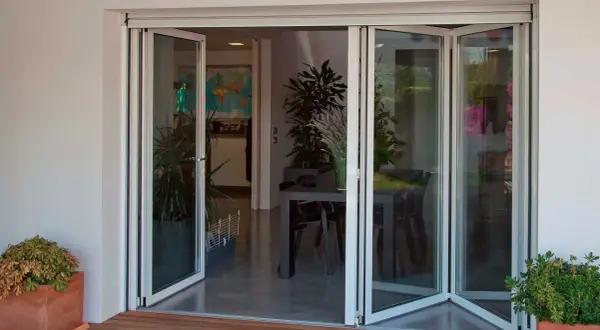 Puertas de cristales plegables que abren a un comedor interior con plantas y una mesa.
