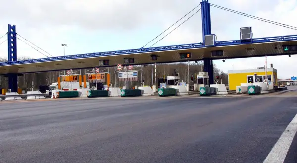 Péage d'autoroute avec plusieurs voies de passage. Une voiture attend à une borne de péage.