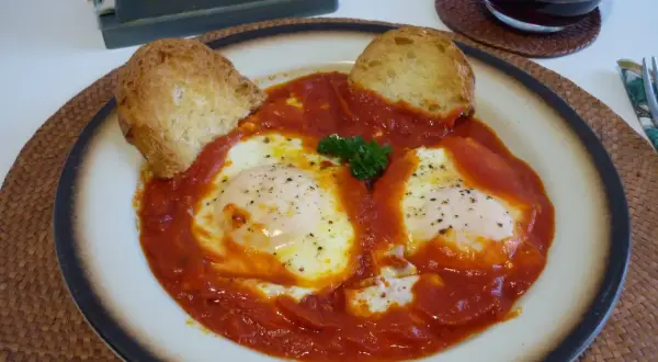 Uova in trippa marchigiana, un piatto saporito con uova cotte nel sugo di pomodoro, guarnito con pane tostato e prezzemolo.