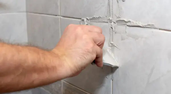 Main tenant utilise un couteau pour refaire joint carrelage.