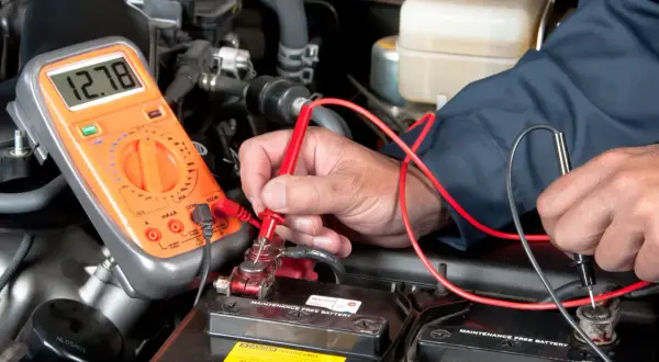 Mechaniker prüft mit Multimeter die Autobatterie, um den Anlasser wechseln zu können.