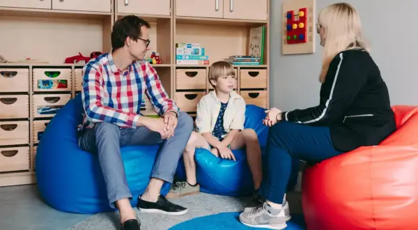 Ojciec, syn i terapeutka rozmawiają w przytulnym pokoju. To ważny moment terapii dla nastolatków, gdzie budowane jest zaufanie i wsparcie.