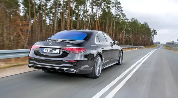 Czarny Mercedes S400d 4Matic sunie po drodze wśród drzew.