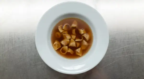 Eine Schüssel mit dampfendem Tortellini in Brodo auf einem metallischen Hintergrund.