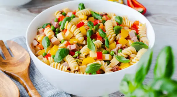 Bunter Nudelsalat ohne Mayo mit Spiralnudeln, Erbsen, Paprika und Schinkenwürfeln, garniert mit Basilikum.