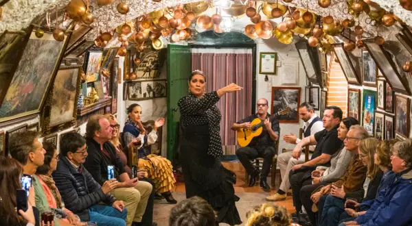 Una bailaora de flamenco, con un guitarrista y público, en un local decorado con cobre. ¡Gracias en flamenco!
