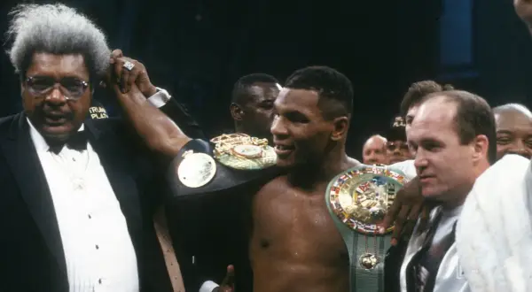 Don King raises Mike Tyson's arm, showcasing championship belts. A triumphant moment for the boxer and his promoter.