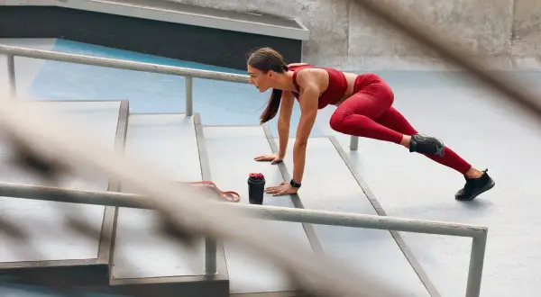 Donna in tenuta sportiva rossa esegue un esercizio per snellire le gambe senza ingrossarle, su una scalinata all'aperto.