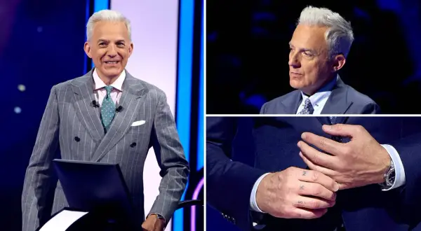 Hubert Urbański w eleganckim garniturze, z widocznym tatuażem na dłoni.