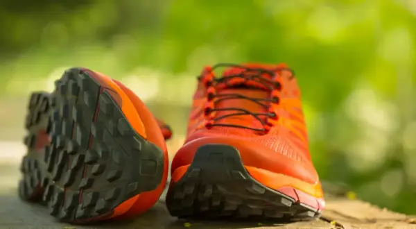 Leuchtend orange Wanderschuhe mit grobstolliger Sohle, bereit, neu besohlt zu werden für neue Abenteuer.