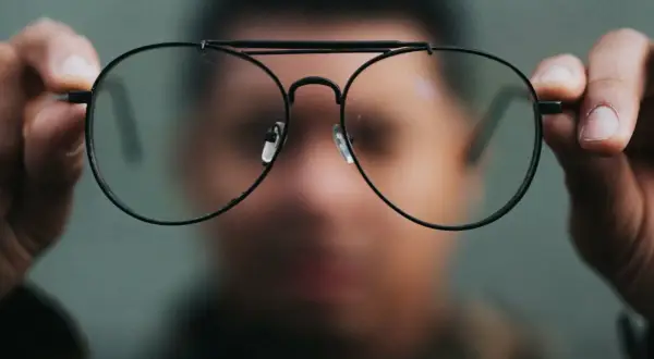 Osoba trzyma przed twarzą okulary. Nowe okulary dziwne widzenie, jakby świat przez nie wyglądał inaczej.