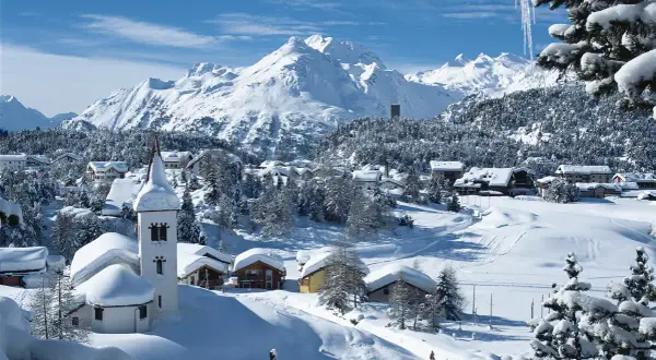 Winteridylle in der Schweiz: verschneite Berge, ein Dorf mit Kirche und Häusern, umgeben von Tannen.
