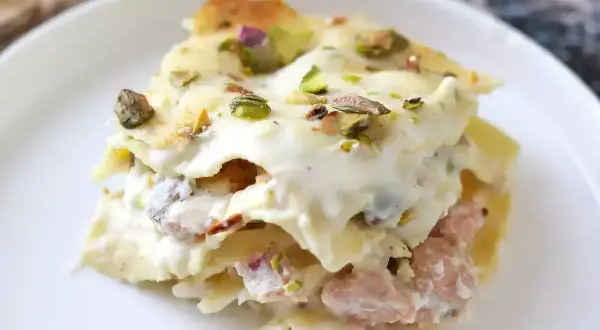 Porzione di lasagne bianche sfiziose con pistacchi e un ripieno cremoso, servite su un piatto bianco.