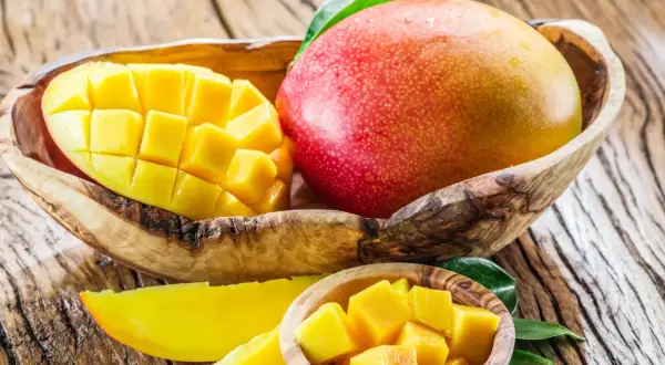 Soczyste mango, pokrojone w kostkę i w całości, w drewnianych miseczkach. Idealne na zdrową przekąskę, z niskim mango kcal.