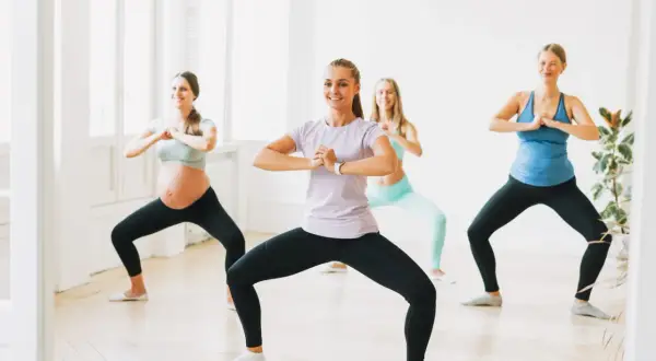 Kobiety wykonują ćwiczenia na nietrzymanie moczu, w tym przysiady. Jedna z nich jest w ciąży.