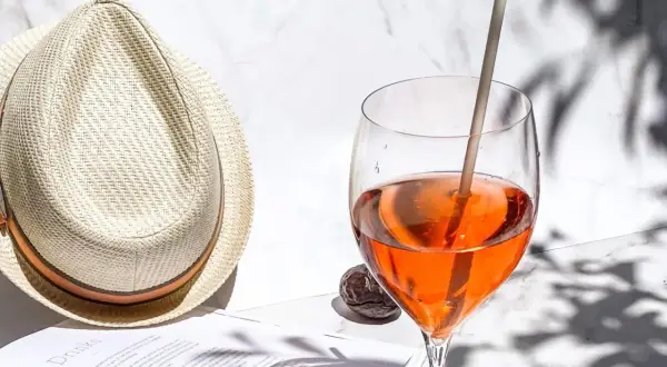 Ein Aperol Spritz im Glas neben einem Strohhut und einem Buch.