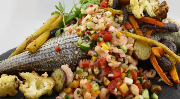 Poisson au barbecue avec salade de crevettes, légumes rôtis et herbes fraîches. Un plat coloré et savoureux.